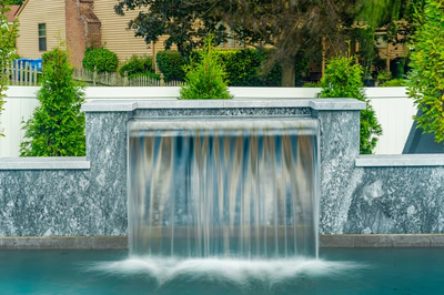 Single-tier natural stone sheer descent waterfall flowing into a pool with lush green landscaping
