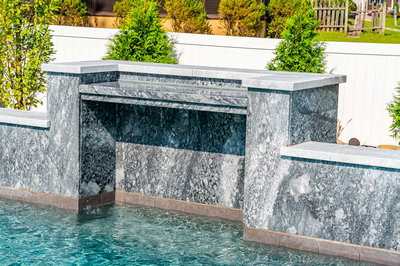 Two-tiered natural stone waterfall cascading into a pool surrounded by lush green garden plants
