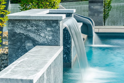 Multi-tiered natural stone boulder waterfalls cascading into a pool with lush garden plants