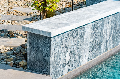 Single-tier natural stone waterfall cascading into a pool with surrounding river rocks and plants