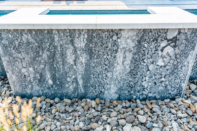 Single-tier natural stone waterfall cascading into a pool with river rocks and ornamental plants