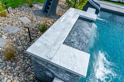 Single-tier natural stone boulder waterfall cascading into a pool with pebbles and small plants