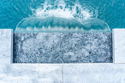 Single-tier natural stone boulder waterfall cascading into a clear pool with lush green plants