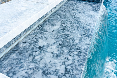 Multi-tiered natural stone boulder waterfall cascading into a swimming pool with surrounding plants