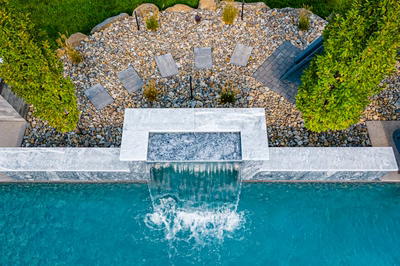 Single-tier stone waterfall cascading into a pool with gravel landscaping and small green trees. (14 words)*   Check constraints:
*   10-15 words