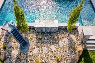 Single tier natural stone waterfall cascading into a pool surrounded by gravel and slender trees