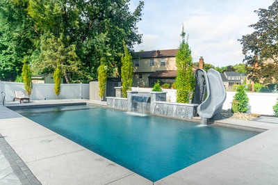Two-tiered natural stone waterfall cascading into a rectangular pool surrounded by tall slender trees