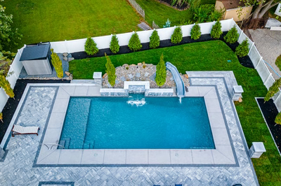 Single-tiered natural stone waterfall cascading into a rectangular pool amidst manicured lawn and evergreens