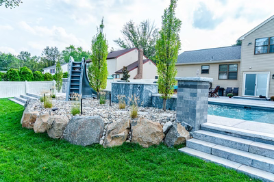 Multi-tiered natural stone boulder waterfall cascading into a pool surrounded by tall trees