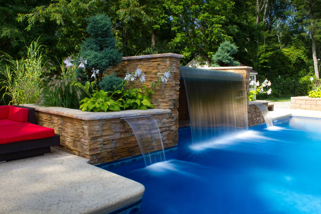 Triple sheer descent waterfalls cascade from stacked stone walls into a pool with lush landscaping