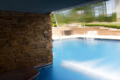 Single-tier natural stone boulder waterfall cascading into a pool with surrounding green plants