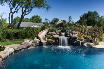 Two-tiered natural stone boulder waterfall cascading into a swimming pool surrounded by lush garden landscaping