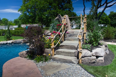 Multi-tiered natural stone boulder waterfall cascading into a pool surrounded by lush garden landscaping
