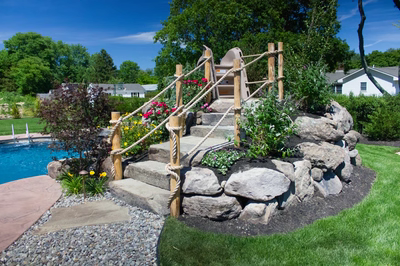 Multi-tiered natural stone boulder waterfall cascading into a pool surrounded by lush garden plants