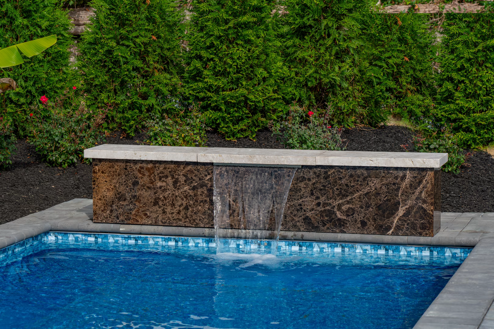 Natural stone waterfall cascading into a pool surrounded by lush green landscaping