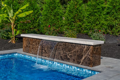 Single-tier natural stone waterfall cascading into a blue pool with lush tropical garden plants