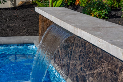 Single-tier natural stone boulder waterfall cascading into a pool with lush background garden plants