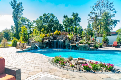 Multi-tiered natural stone boulder waterfall cascades into a freeform pool with lush garden landscaping