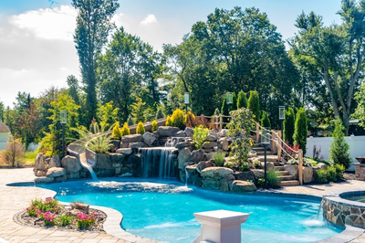 Multi-tiered natural stone boulder waterfall cascading into a clear pool with lush garden landscaping