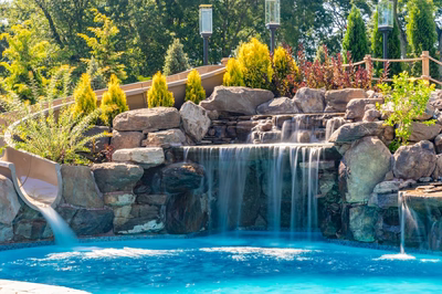 Two-tiered natural stone boulder waterfall cascading into a pool surrounded by lush garden landscaping