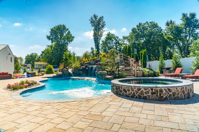 Two-tiered natural stone boulder waterfall cascading into a freeform pool surrounded by lush plants