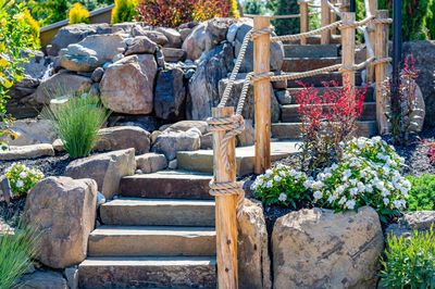 Multi-tiered natural stone boulder waterfall cascading into a pool surrounded by vibrant garden plants