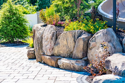 Multi-tiered natural stone boulder waterfall cascading into a pool area with vibrant garden landscaping