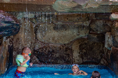 Single-tier natural stone boulder waterfall dripping into a blue tiled pool with swimming children