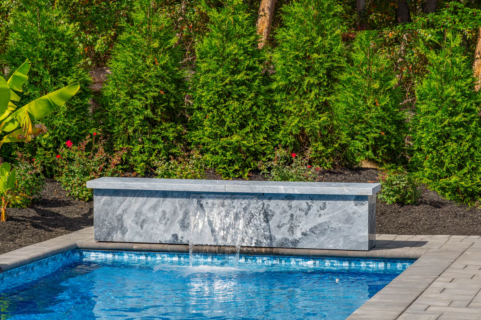 Natural stone waterfall cascading into a rectangular pool surrounded by lush green plants
