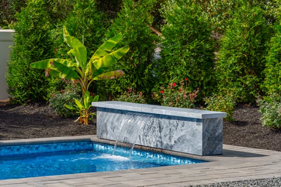Single-tier natural stone waterfall with sheet flow into a pool beside tropical plants