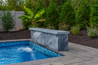 Single-tier marble block waterfall cascading into a pool surrounded by banana plants and evergreens