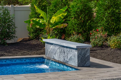 Single-tier natural stone waterfall cascading sheet-like into a pool surrounded by lush tropical plants