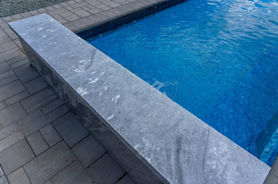 Single-tier natural stone feature with gentle water flow into a pool and patio