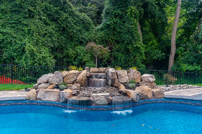 Three-tiered natural stone boulder waterfall cascading into a pool surrounded by dense green foliage