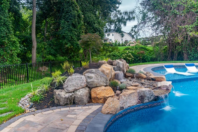 Multi-tiered natural stone boulder waterfall cascading into a blue pool surrounded by lush greenery