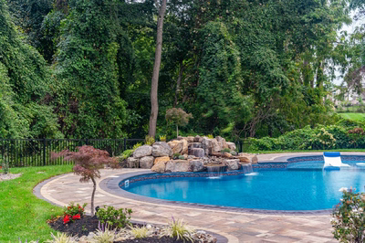 Multi-tiered natural stone boulder waterfall cascades into a pool surrounded by lush garden landscaping
