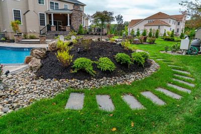 Multi-tiered natural stone waterfall cascading into a pool surrounded by mulch and green plants