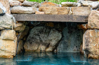 Multi-tiered natural stone boulder waterfall cascading into a pool with lush green plants