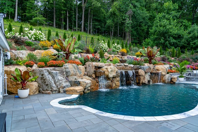 Multi-tiered natural stone boulder waterfall cascading into a pool surrounded by lush, vibrant landscaping