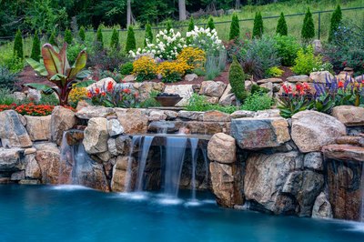 Multi-tiered natural stone boulder waterfalls cascade into a pool surrounded by lush garden landscaping