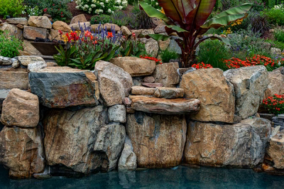 Multi-tiered natural stone boulder waterfall cascading into a pool surrounded by lush tropical plants