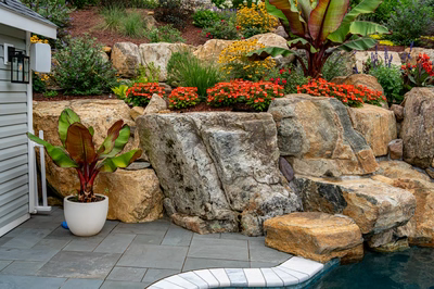 Multi-tiered natural stone boulder waterfall cascading into a pool surrounded by lush tropical plants