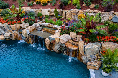 Multi-tiered natural stone boulder waterfalls cascading into a pool surrounded by lush tropical plants