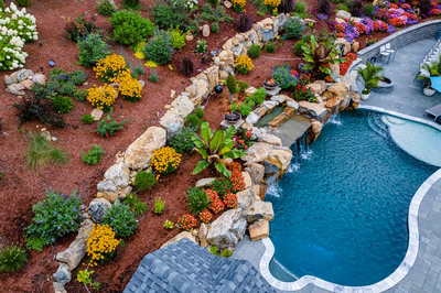 Multi-tiered natural stone boulder waterfall cascading into a freeform pool with vibrant tropical landscaping