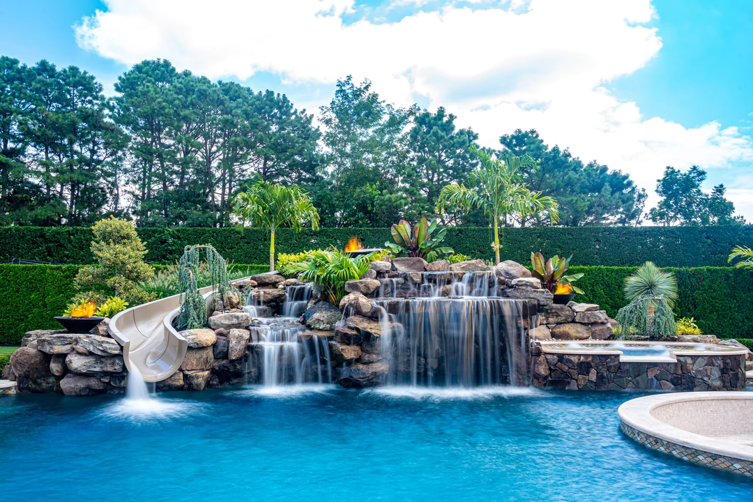 Multi-tiered natural stone boulder waterfalls cascade into a pool surrounded by lush tropical landscaping