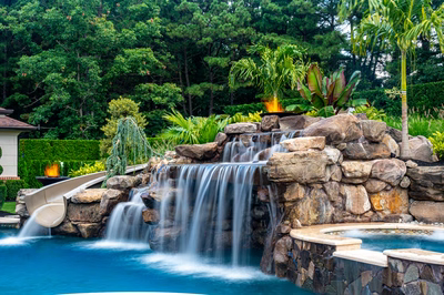 Multi-tiered natural stone boulder waterfall cascading into a pool with lush tropical landscaping