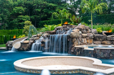 Cascading multi-tiered natural stone boulder waterfall flowing into a pool with lush tropical greenery