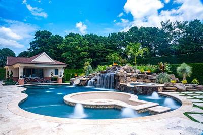Multi-tiered natural stone boulder waterfalls cascade into a freeform pool with lush tropical landscaping