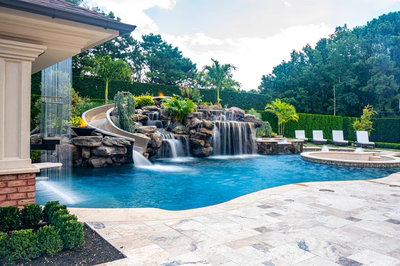 Multi-tiered natural stone boulder waterfall cascading into a blue pool with lush tropical landscaping