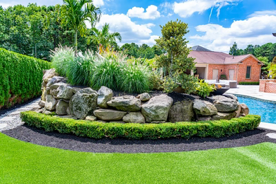 Multi-tiered natural stone boulder waterfall cascading into a pool surrounded by lush tropical greenery